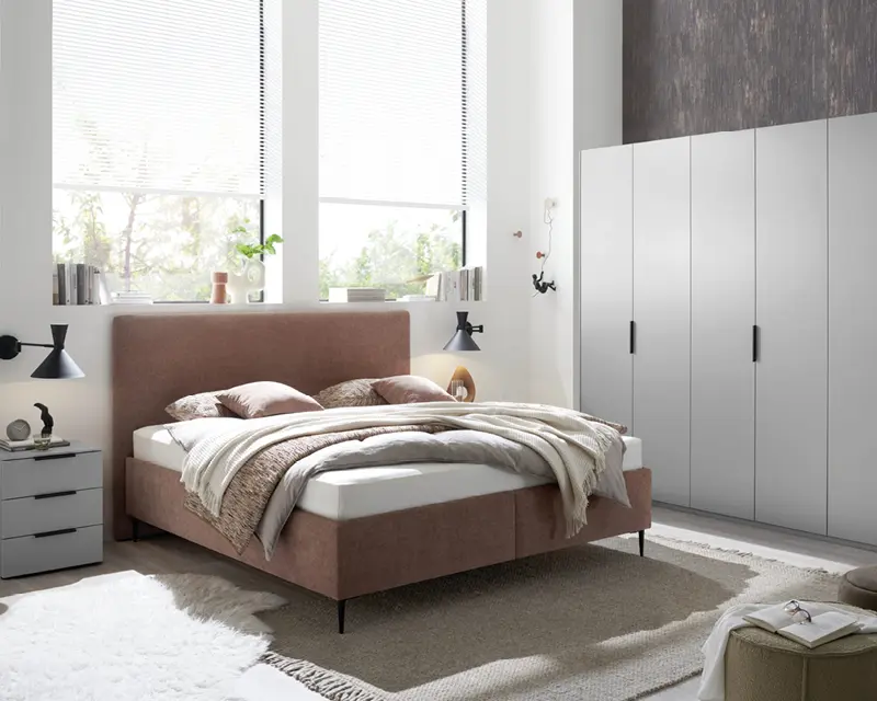 Schlafzimmer mit Polsterbett, Nachttisch, grauem Kleiderschrank und hellem Teppich